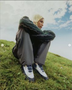 a man sitting on top of a green grass covered field next to a blue sky