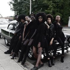 a group of women standing next to each other on the side of a road in front of a car