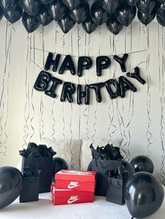 balloons and gifts on a bed with the words happy birthday written in black balloon letters