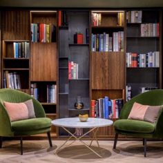 two green chairs sitting next to each other in front of a book shelf filled with books