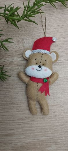 a brown teddy bear ornament hanging from a tree branch on a wooden surface