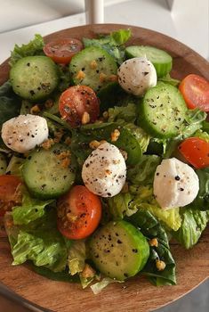 a salad with cucumbers, tomatoes and other toppings on a wooden plate