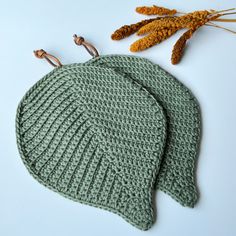 two knitted hats sitting on top of each other next to dried flowers and scissors