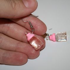 a person holding a tiny pink object in their hand next to a pair of earrings