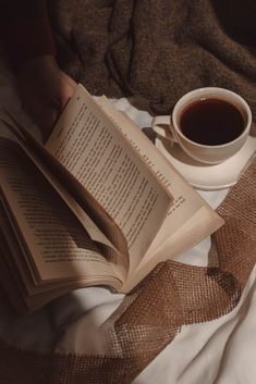 an open book sitting on top of a bed next to a cup of coffee