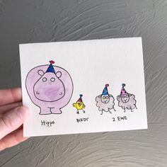 a hand holding up a card with three cartoon animals wearing birthday hats on it's head