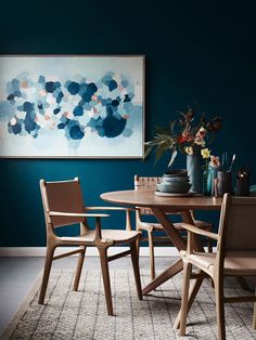 a dining room table with chairs and vases on top of it in front of a blue wall