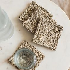 three woven coasters sitting on top of a white marble table next to a glass vase