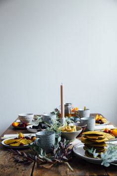 a wooden table topped with plates and bowls filled with food next to a lit candle