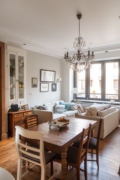 a living room filled with furniture and a chandelier above a wooden dining table