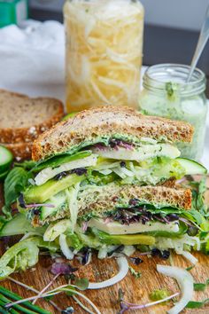 a cut in half sandwich sitting on top of a cutting board next to a jar of pickles