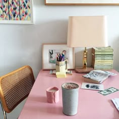 a pink desk topped with a cup of coffee next to a lamp and pictures on the wall