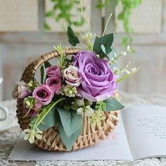 a basket filled with flowers sitting on top of a table next to an open book