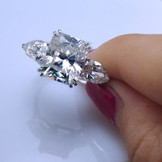 a woman's hand holding an engagement ring with three pear shaped diamonds