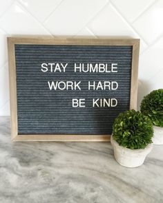 a sign that says stay humble work hard be kind next to two potted plants