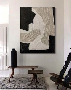 an abstract painting hangs on the wall next to a wooden bench and table in a white room