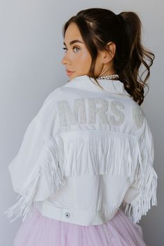 The Dallas Fringe is a cropped style white denim jacket with fringe tassels. Nice and light-weight - super comfortable. *Pearl Patch and Varsity Patches sold seperately* SIZE INFO Cropped fit S=0-4, M=6-10, L=12-14. DETAILS & CARE Front button closure Spread collar Chest button-flap pockets 100% cotton Hand wash/Spot Clean only to avoid patches coming off. Imported FINAL SALE Mrs Jean Jacket, Fringe Dress Outfit, Denim Jacket With Fringe, Fringe Wedding Dress, Sparkle Jeans, Untamed Petals, Beaded Fringe Dress, Tassel Jacket, Bride Jacket