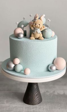 a blue cake with a teddy bear sitting on top of it and decorations around the edges