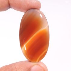 a close up of a person's hand holding an orange object in front of a white background