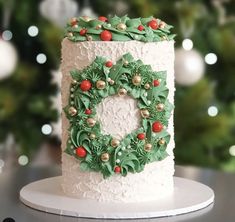 a christmas cake decorated with holly wreaths and berries on a table in front of a christmas tree