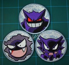 three purple and black cartoon character patches on a green surface with blue squares in the background