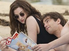 a man and woman laying on the beach reading a magazine