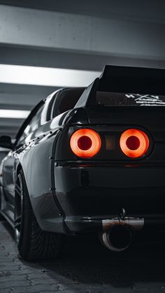 the rear end of a black car with its lights turned on in a parking garage