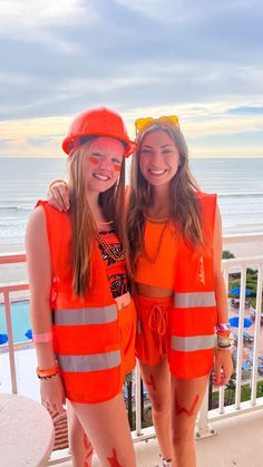 two girls in orange safety vests standing next to each other on a balcony overlooking the beach