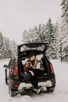 a man and woman sitting in the back of a car with snow on the ground