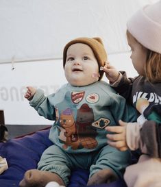 two young children sitting on top of a beanie hat and playing with each other