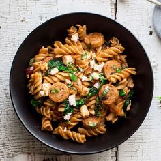 a black bowl filled with pasta and spinach on top of a white wooden table