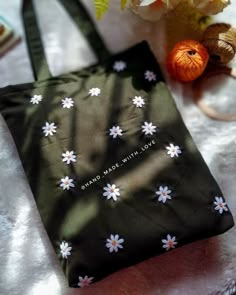 a black bag with white daisies on it sitting next to some flowers and yarn