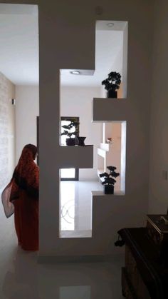 a woman standing in front of a white wall with plants on it and a mirror behind her