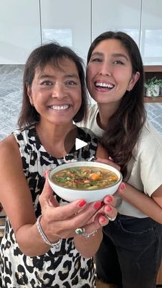 two women are smiling while holding a bowl of soup