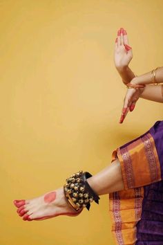 a woman's legs with painted nails and bracelets on her feet, in front of a yellow background