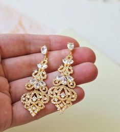 a pair of gold - toned earrings with clear crystal stones is held in a person's hand