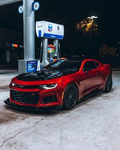 a red chevrolet camaro is parked at a gas station