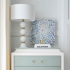 a white dresser topped with a lamp next to a painting