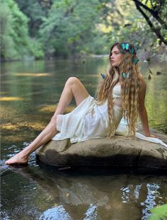 a woman with long hair sitting on a rock in the water wearing a white dress