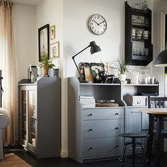 a living room filled with furniture and a clock on the wall over a desk in front of a window