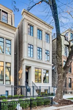 two story apartment building with wrought iron fence and trees on the sidewalk in front of it