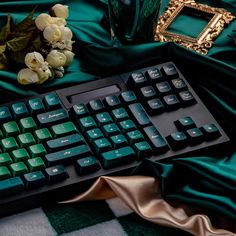 a computer keyboard sitting on top of a green blanket next to a vase with flowers