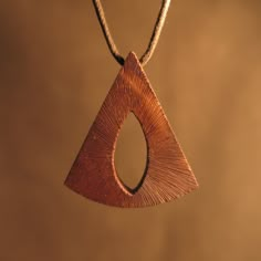 a wooden pendant hanging from a cord on a brown background with the shape of a triangle