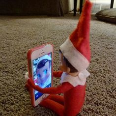 an elf sitting on the floor with a cell phone in front of him and looking at it