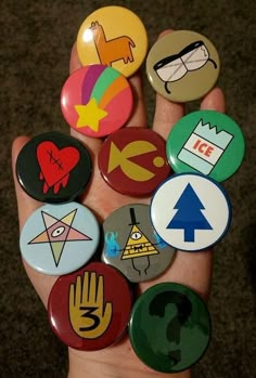 a hand holding several different colored badges in it's palm, all with symbols on them