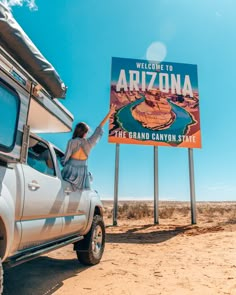 a woman standing on the back of a truck next to a sign that reads welcome to arizona