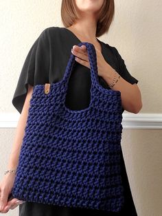 a woman holding a blue crocheted bag in front of her face and smiling