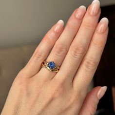 a woman's hand holding a ring with a blue stone on it and gold band