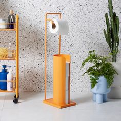 two orange stands with toilet paper on them next to a potted plant and other items