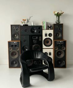 a black chair sitting in front of speakers on top of a white floor next to a wall